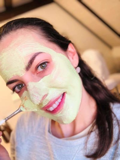 Lachende Frau imt grüner Gesichtsmaske im Gesicht